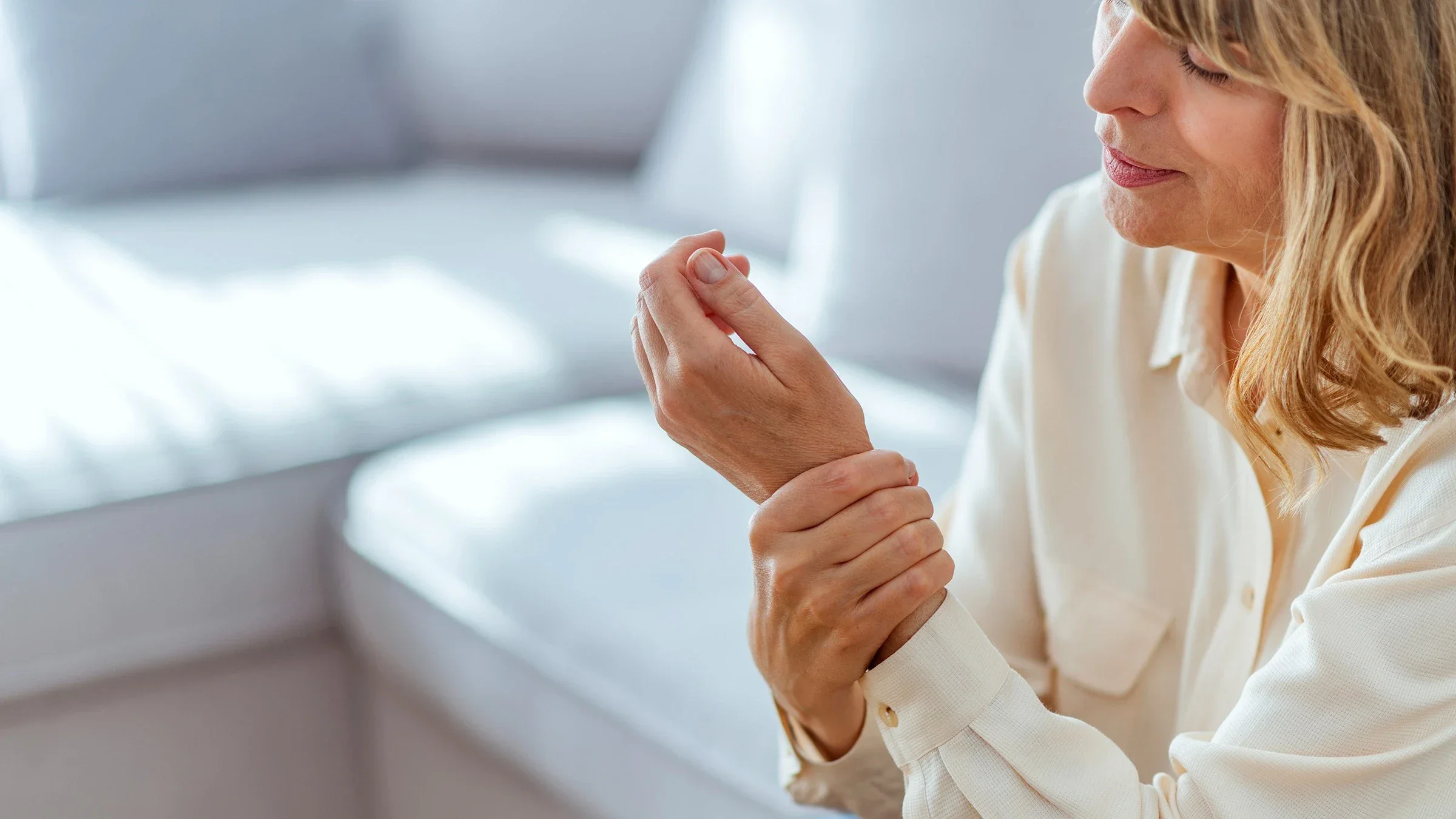 Cropped shot of a woman rubbing her wrist from joint pain. She is sitting on her couch in the living room.
ljubaphoto/E+ via Getty Images
