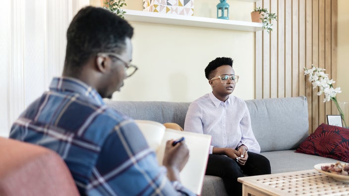 Young female patient sitting on a therapist's couch while the male therapist takes notes.
