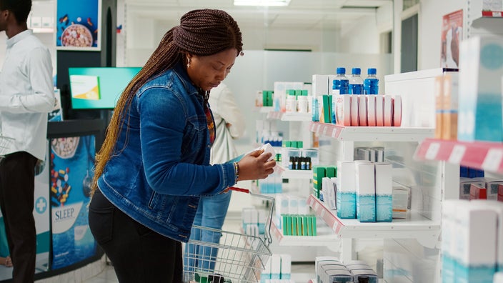 A woman in a pharmacy reads the label on a box of probiotics for vaginal health.