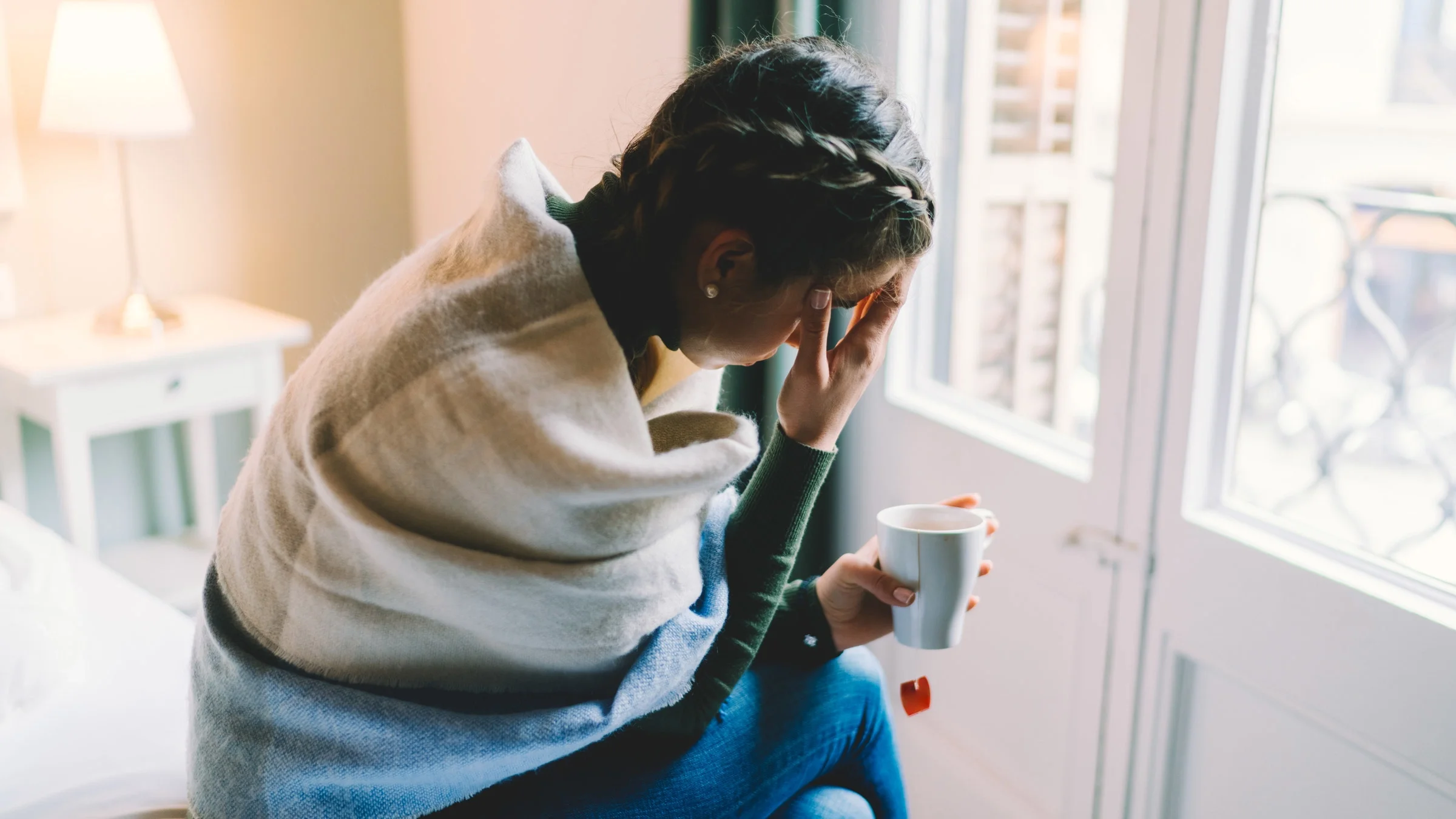 A sick, stressed out person wearing a scarf and drinking tea. 