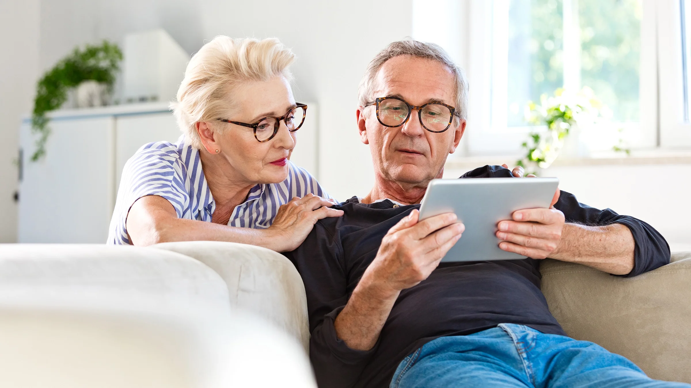 A senior couple looks attentively at a digital tablet at home.