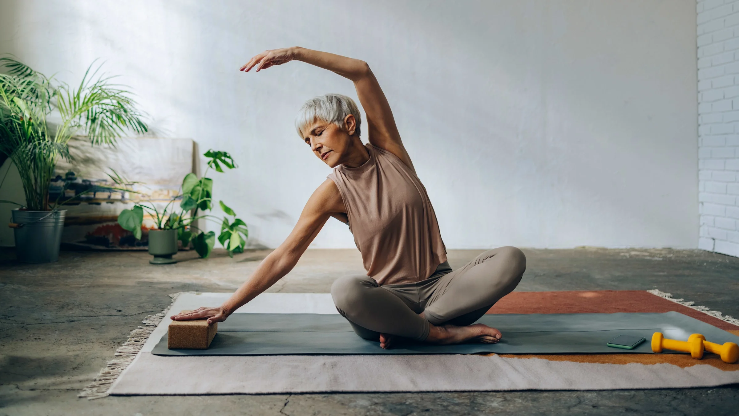 A senior woman doing yoga stretches. There are weights on the yoga mat.