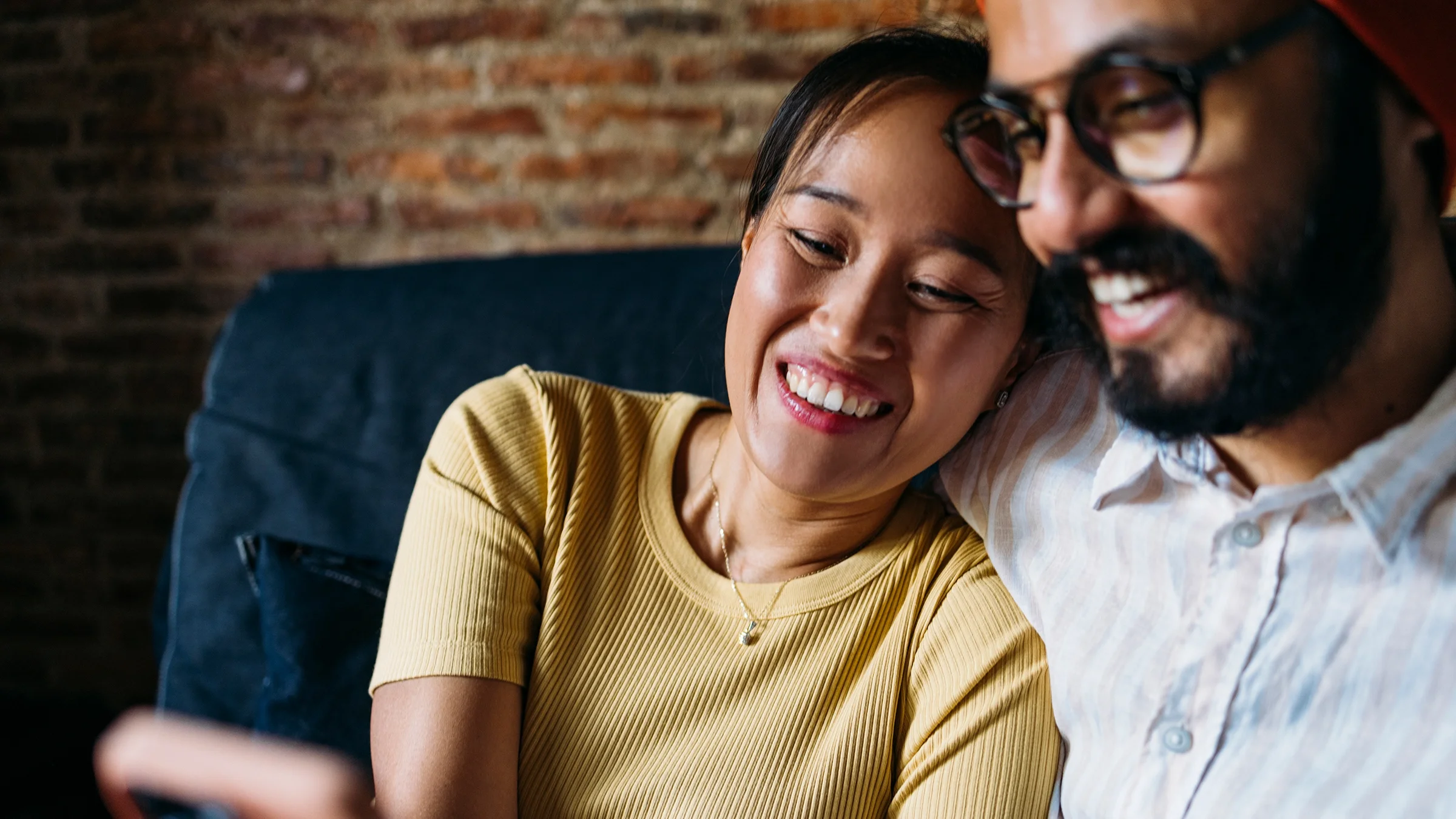 A couple is cuddled up and looking at a smartphone together at home.
