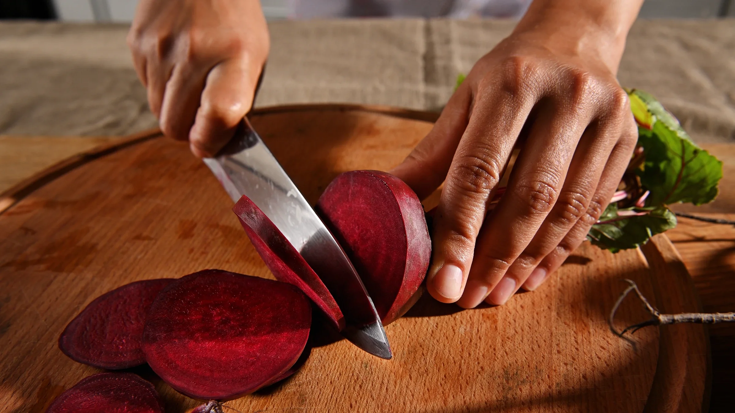 A person cuts beets on the chopping board. 
