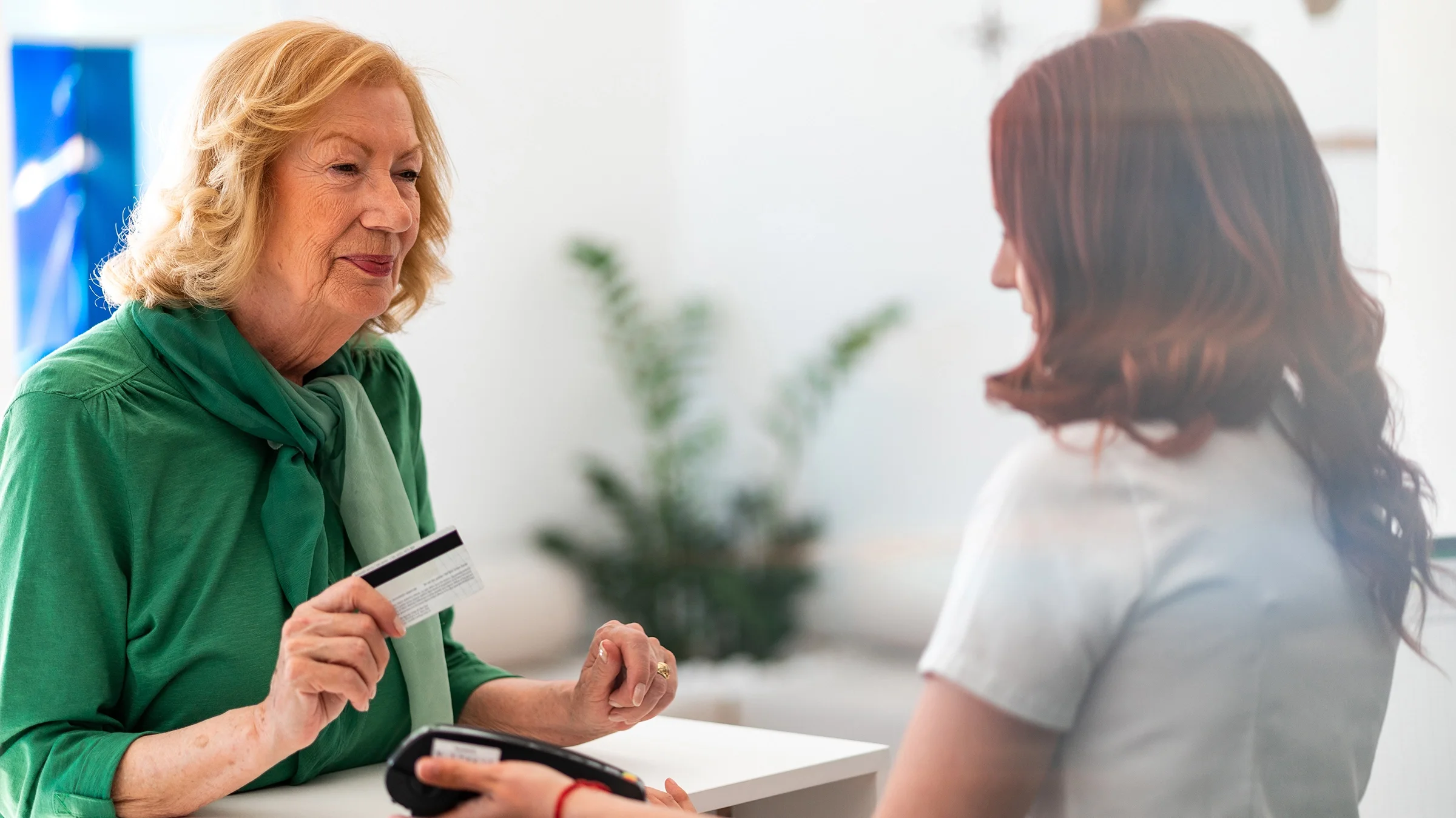  A senior woman uses a credit card to pay at a medical clinic.