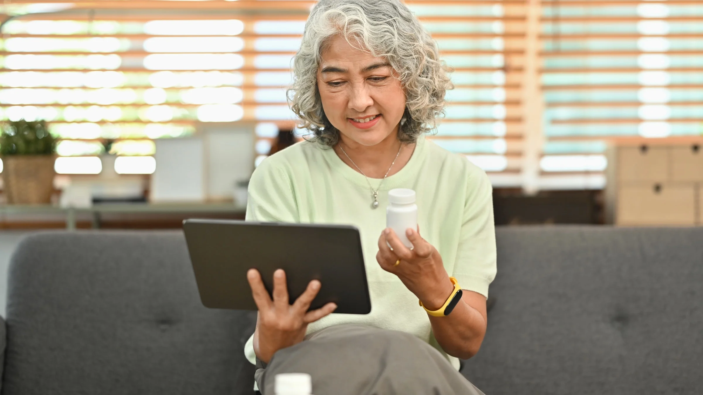 An older woman holding a computer tablet and a pill bottle.