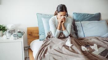 Health: Medication education: woman blowing nose on bed-1134952664