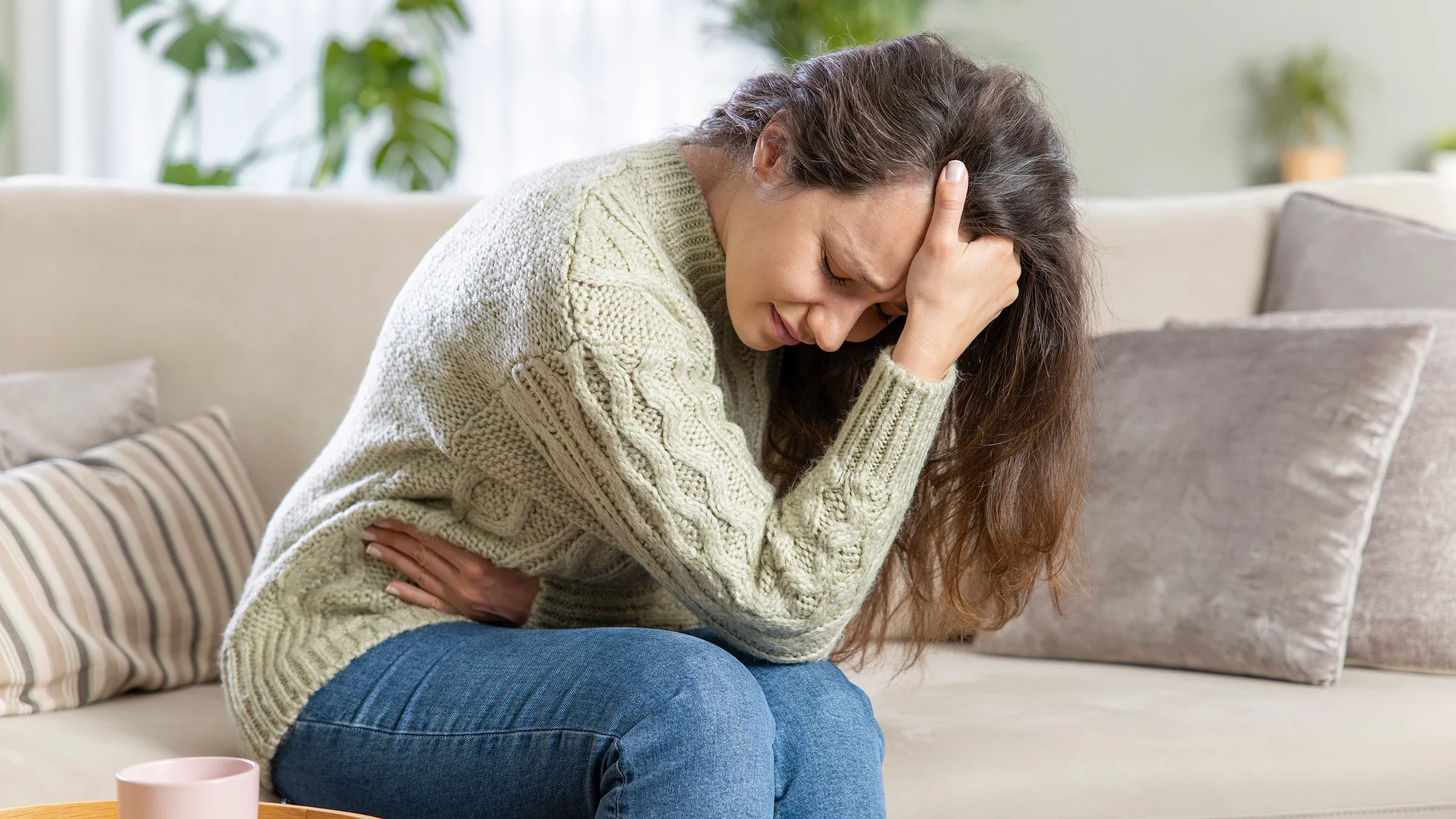 Woman bent over, resting her head in her hand. She is grabbing her stomach with the other as if she is in pain.
eternalcreative/iStock via Getty Images