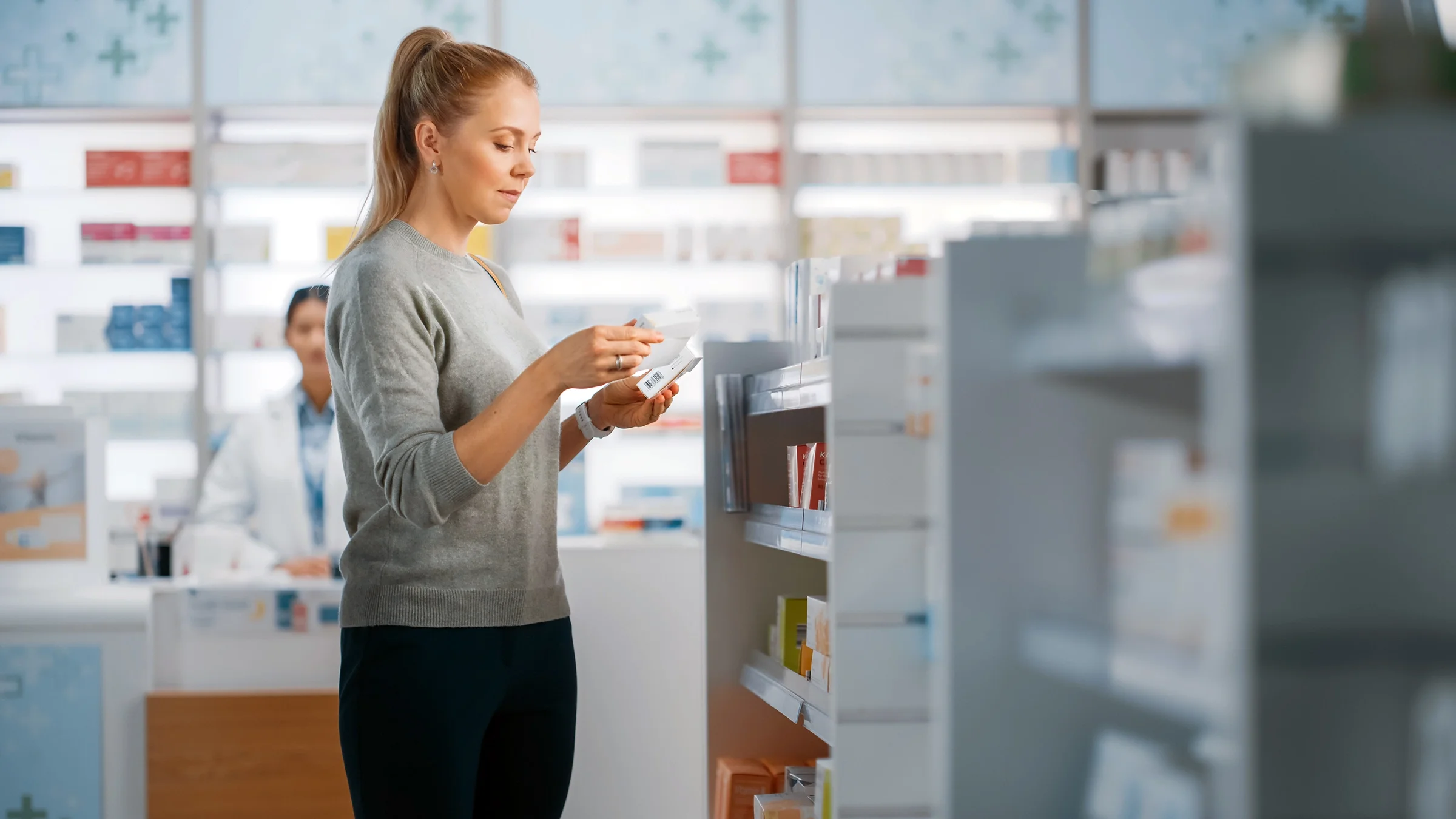 A woman reads an Rx box inside of a pharmacy.