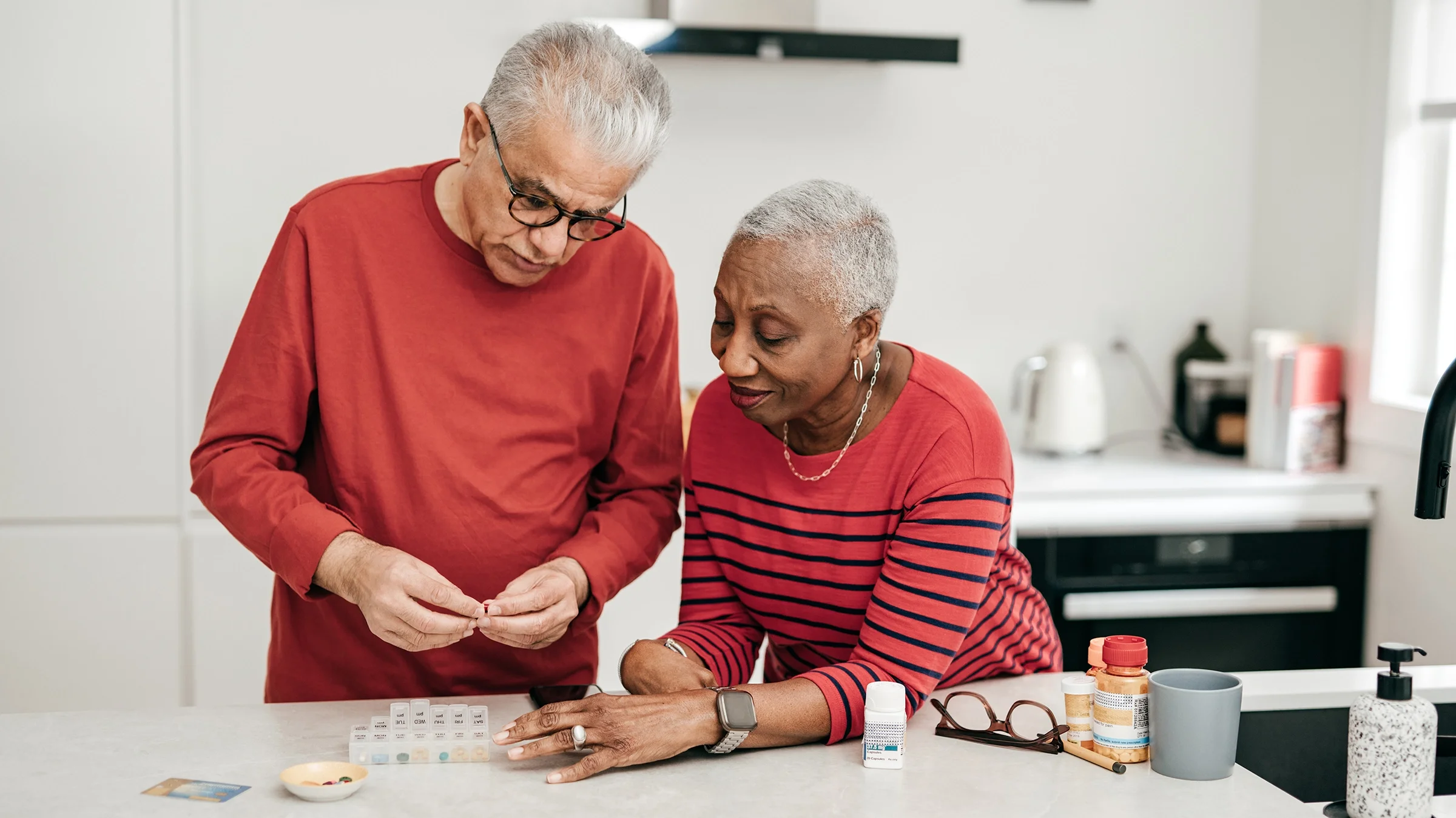 Senior couple, both wearing red, going over medication and scheduling with a pill organizer.