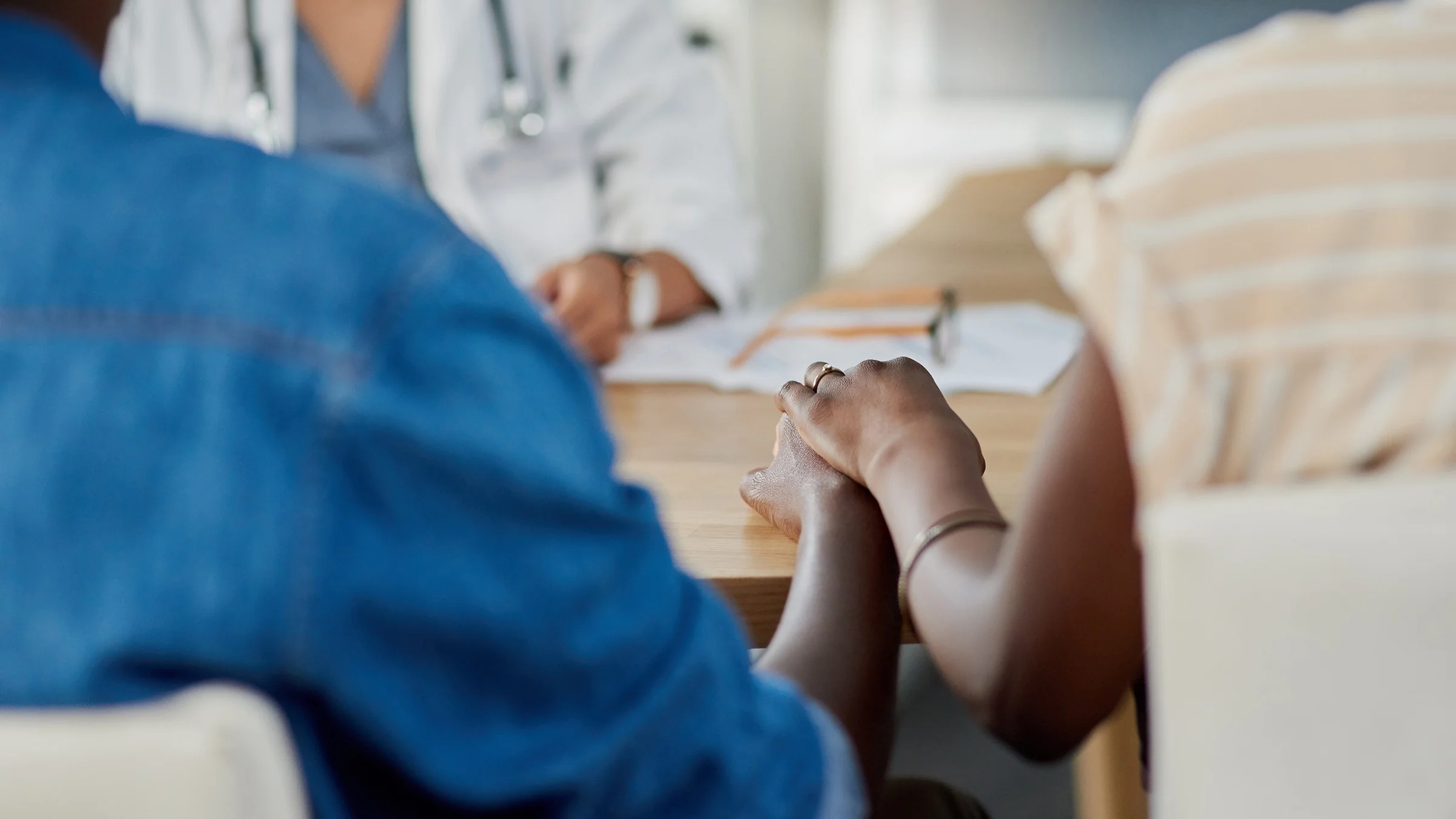 A close-up of a couple holding hands at the doctor's office waiting for results.