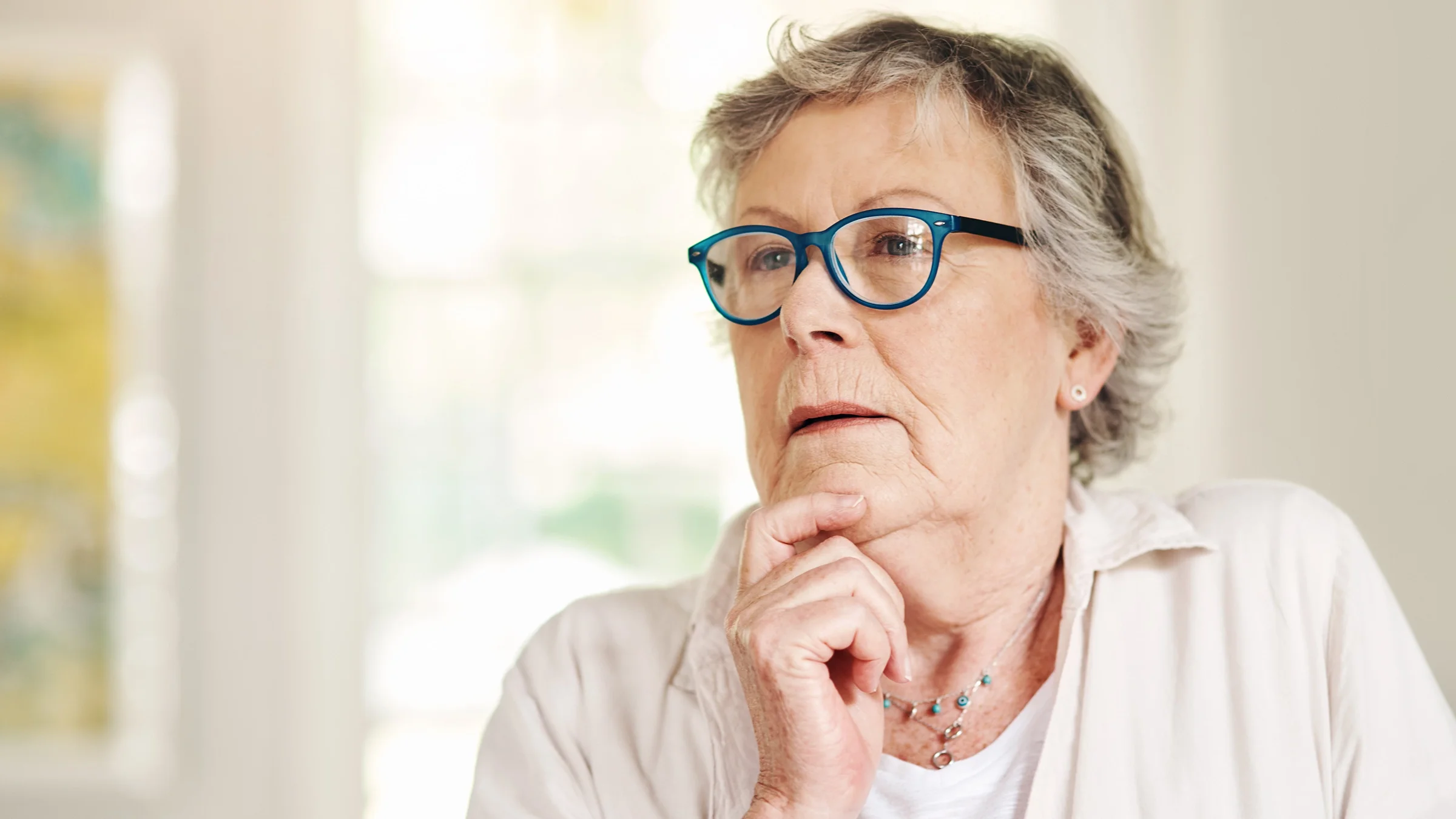 Portrait of a senior woman with blue glasses looking contemplative with her hand on her chin.