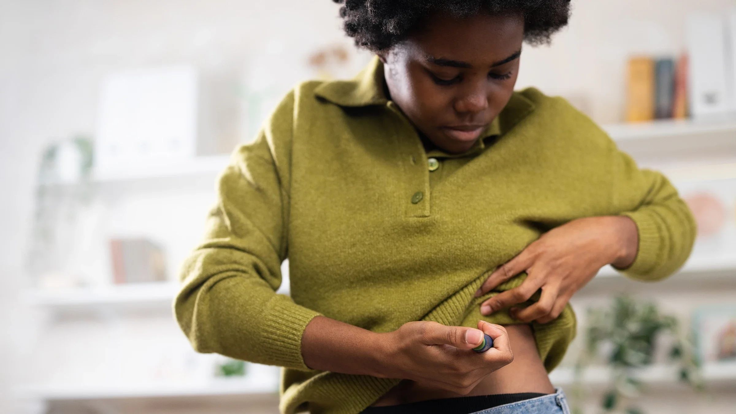A woman is administering an insulin injection into her abdomen at home.
