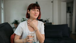 Woman at home grimacing and holding a glass of water.
Brothers91/E+ via Getty Images