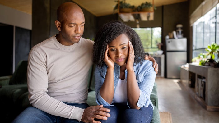 A husband consoles his worried wife at home.