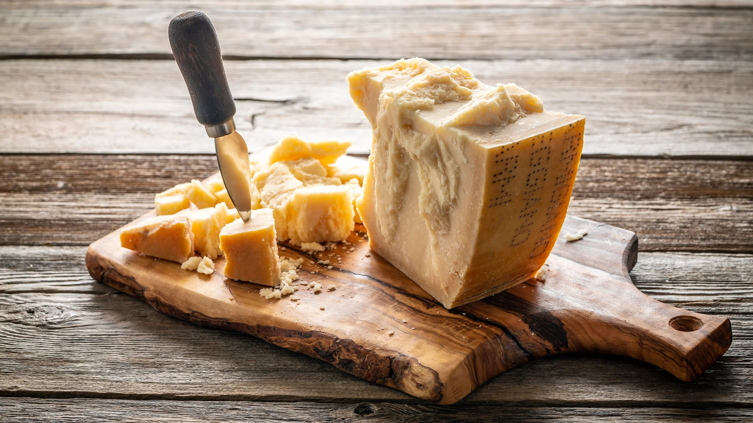 Parmesan Reggiano cheese and cutting board with knife on a wooden table