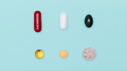 Six different supplement pills of various shapes, sizes, and colors laid flat on a light blue background.