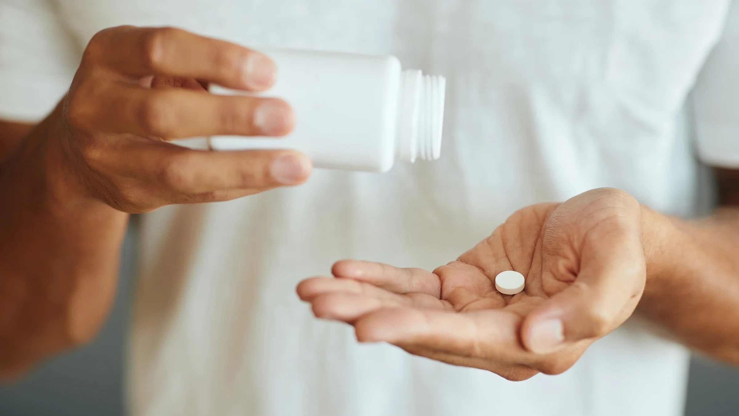 Cropped close-up of a person pouring a pill into their hand.