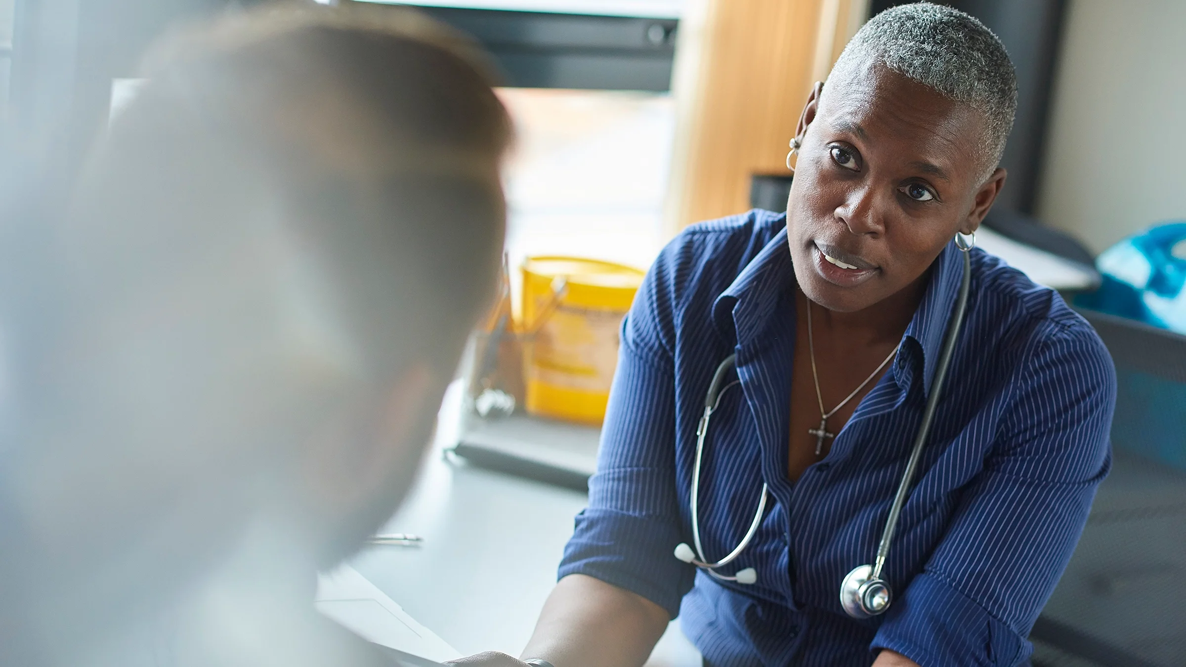 Doctor talking seriously with a patient. The patient is out of focus from behind.