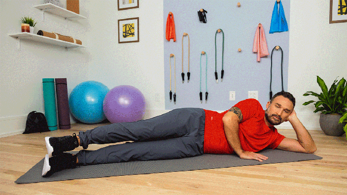 Man lifting straight leg and demonstrating side lying leg lift exercise while laying on a yoga mat.