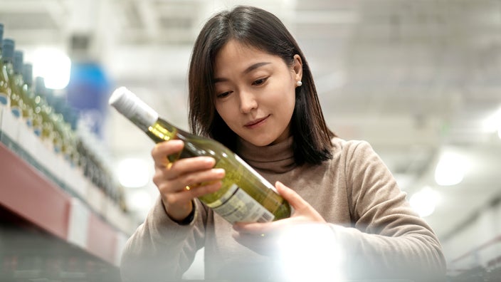 A woman is looking at a wine bottle label in the store.