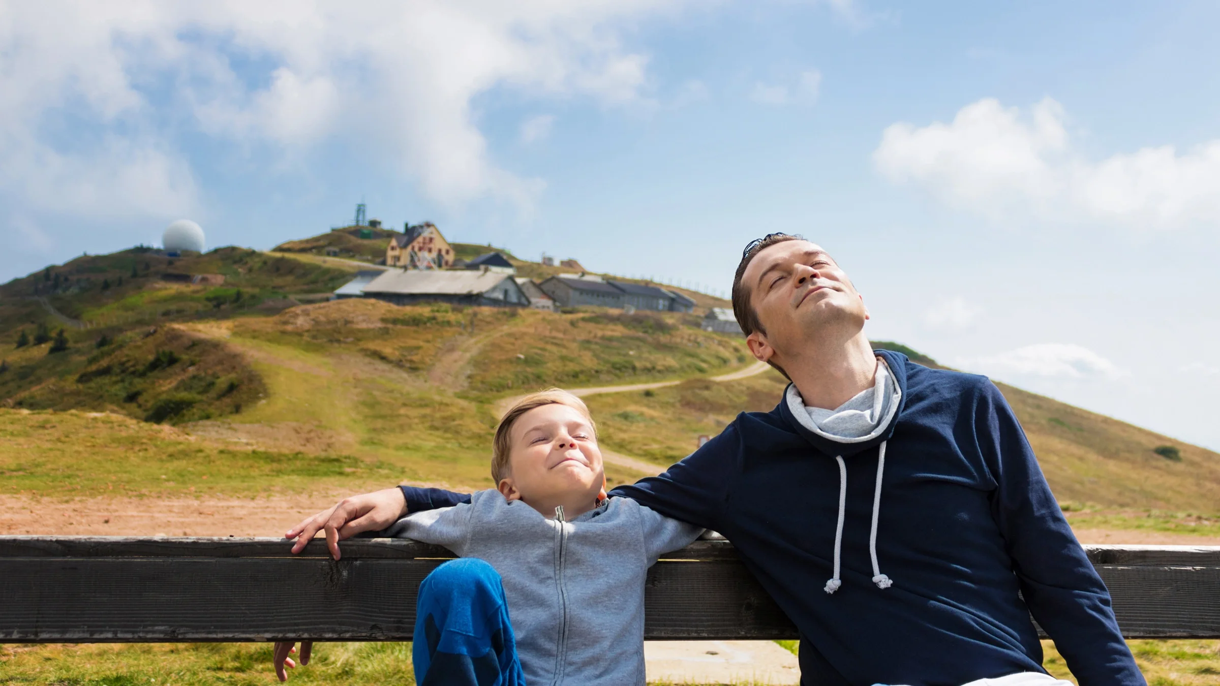 Father and son out on a sunny day having a mindful moment on a park bench.
