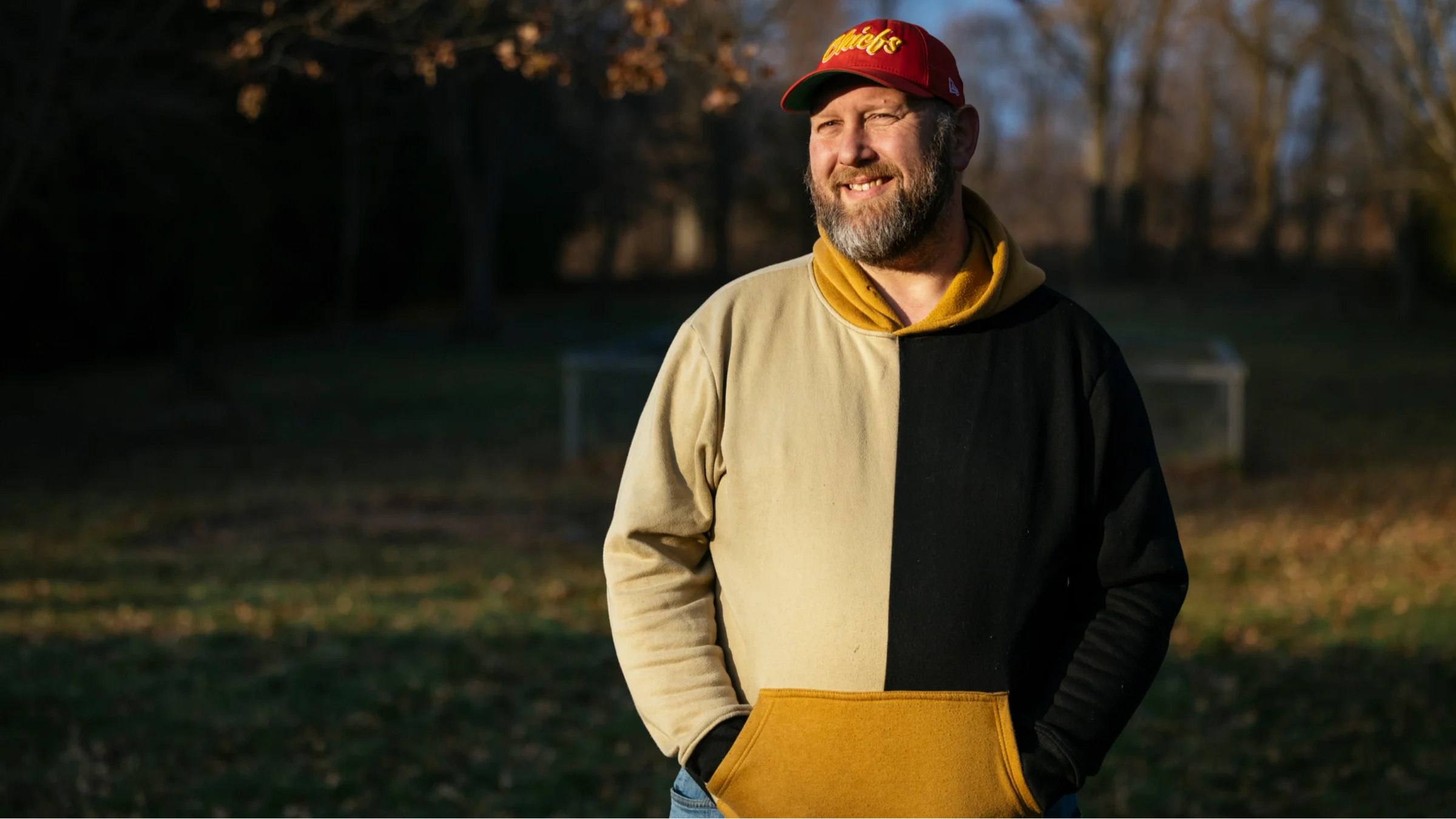 Steve Willis smiling on a crisp fall day outdoors. He is wearing a sweatshirt and a Chiefs baseball cap.