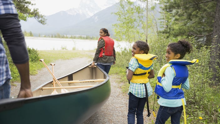A family carries a canoe towards a lake.