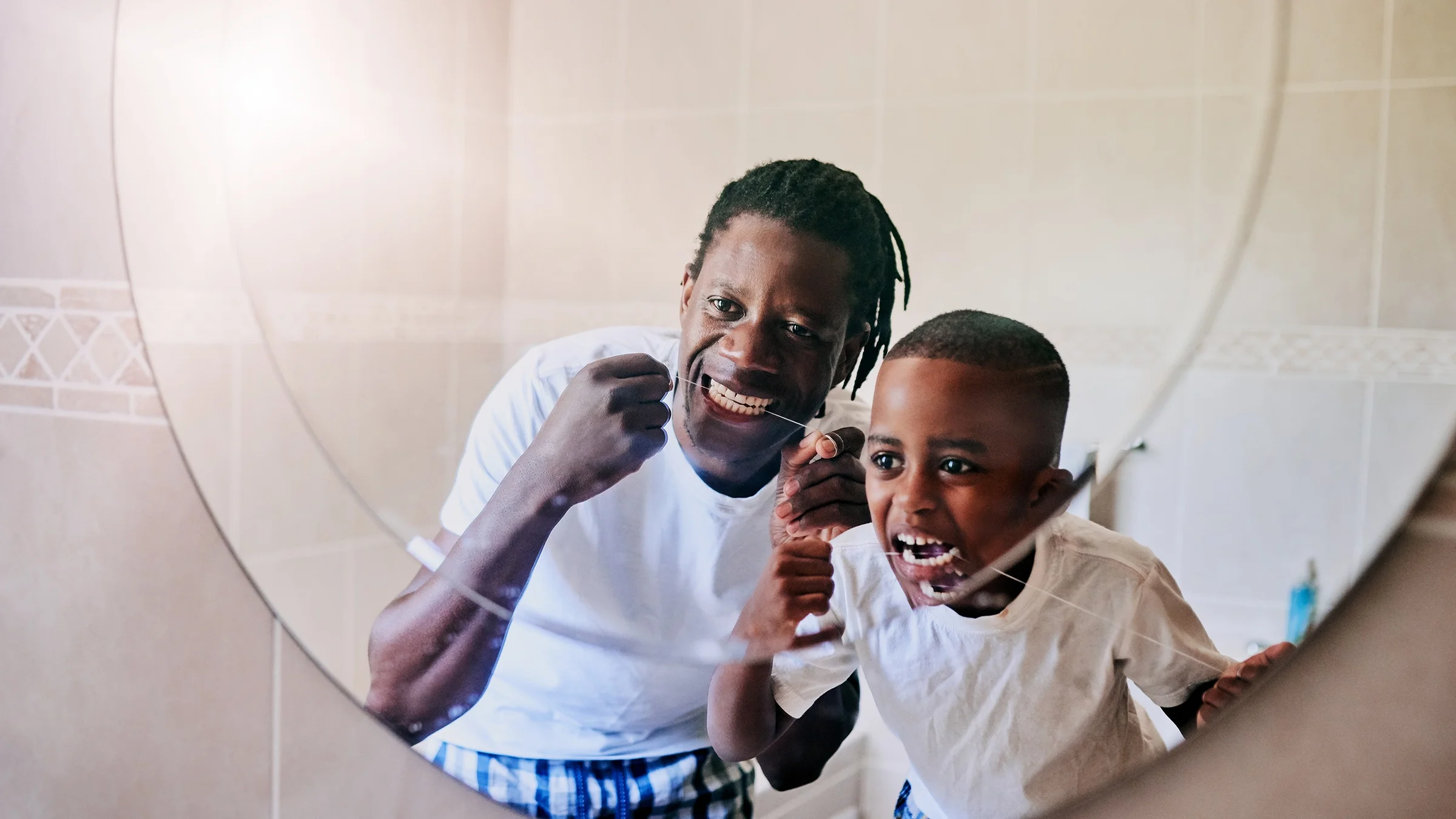 A parent and their child are flossing their teeth in the bathroom.