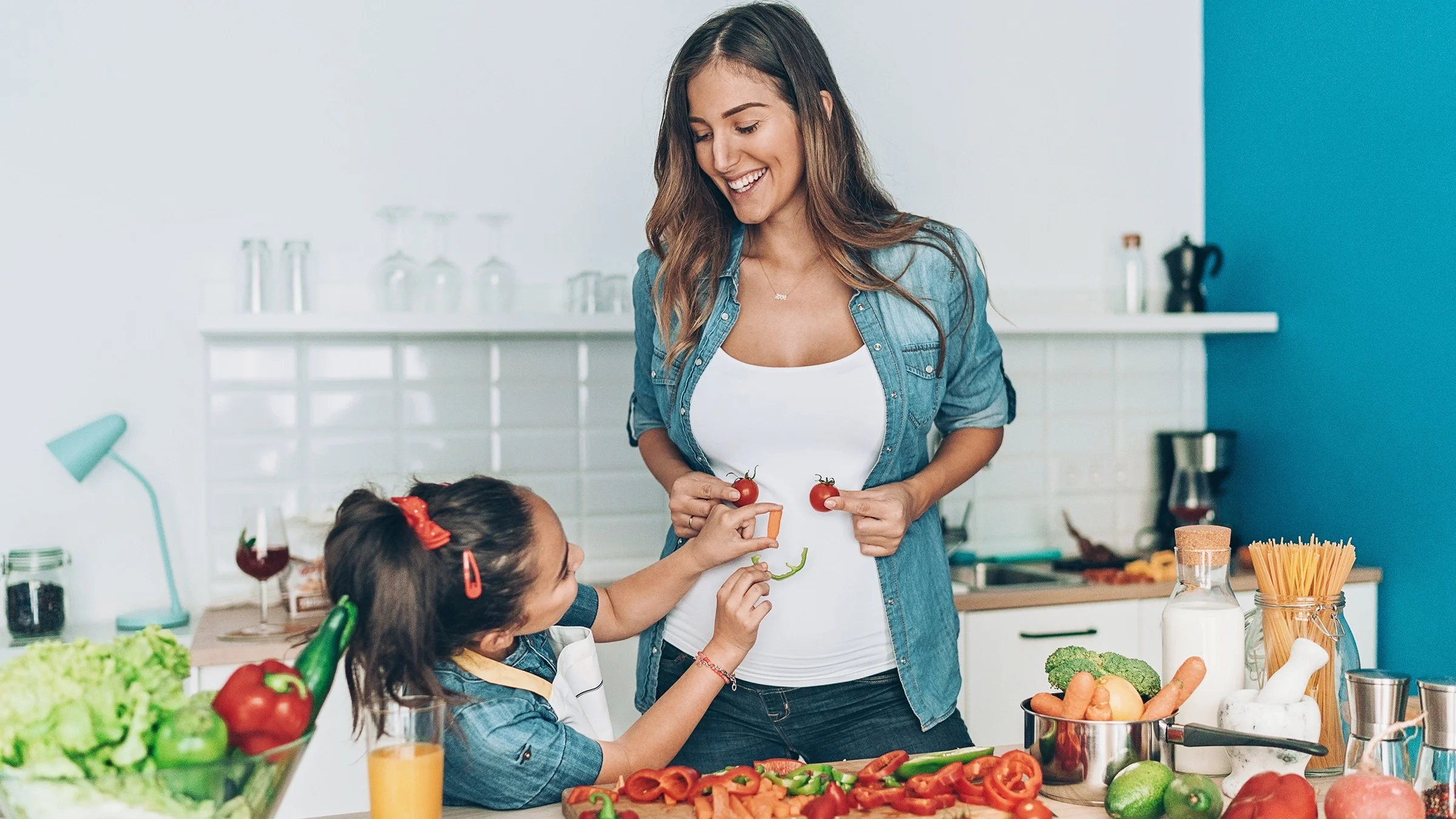 Young mom prepping veggies for dinner with her daughter. They are having fun and being silly and making a smiley face out of the veggies.