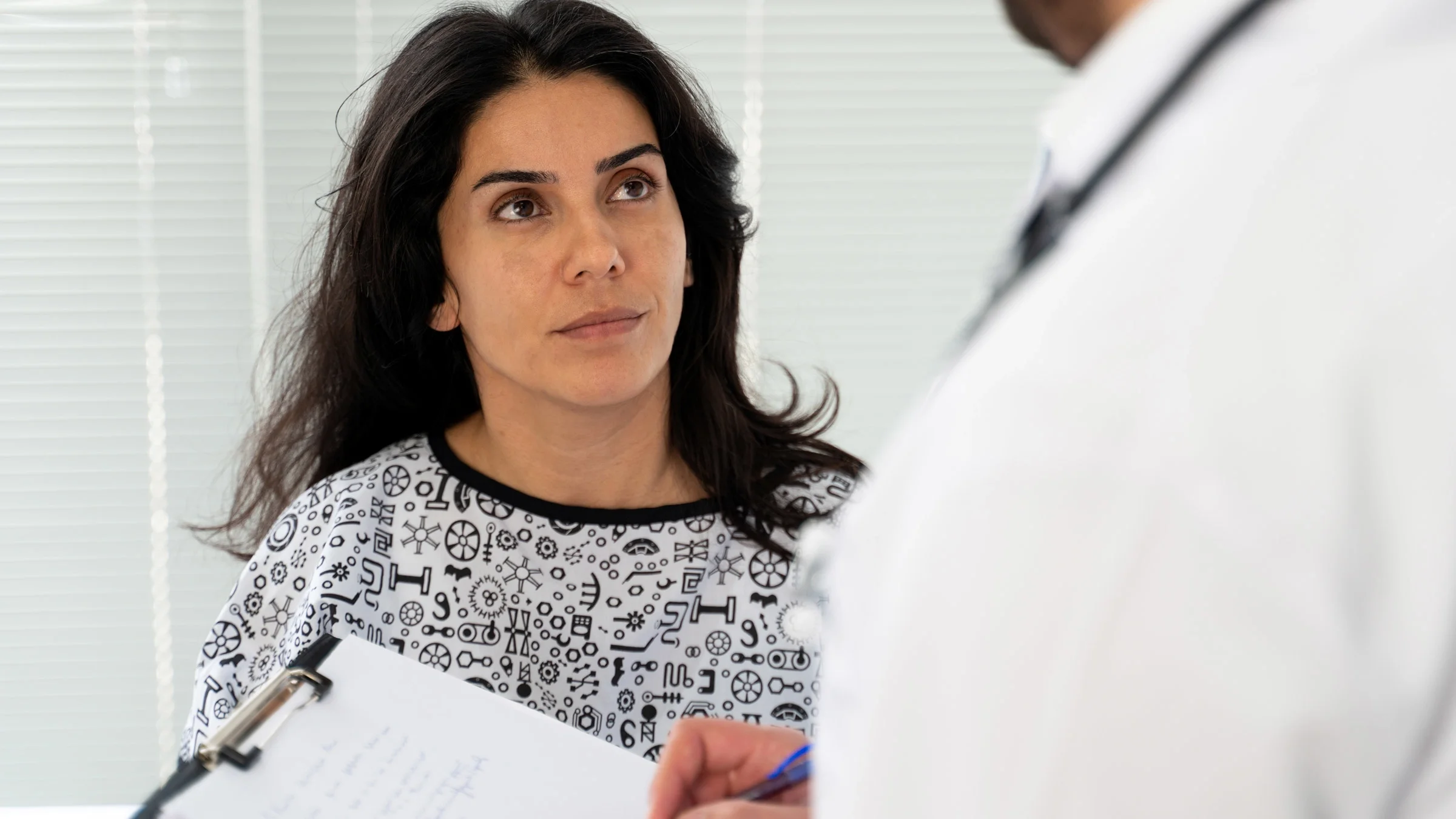 A patient looking at a HCP, who is taking notes on a clipboard.
