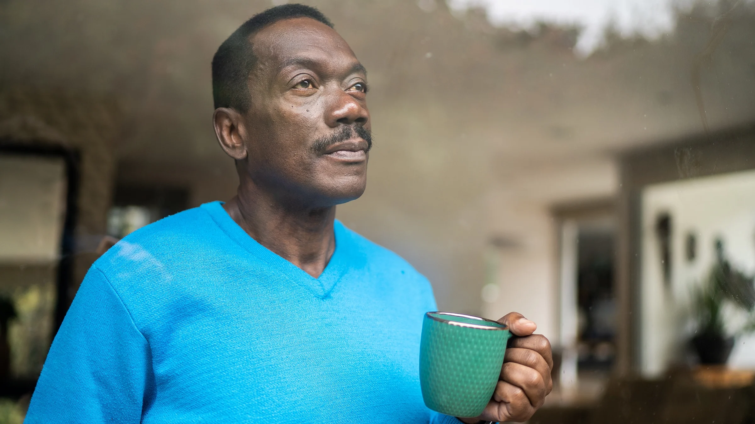 Older man drinking a cup of coffee and looking out the window.