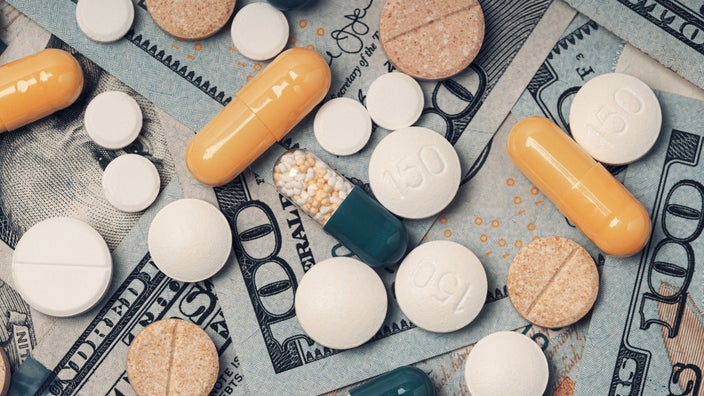 Close-up of various pills that are white, orange, and green on a pile of hundred dollar bills.