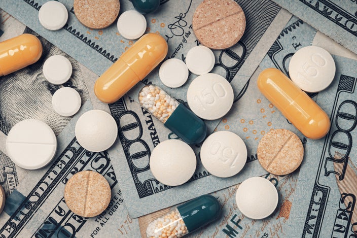 Close-up of various pills that are white, orange, and green on a pile of hundred dollar bills.