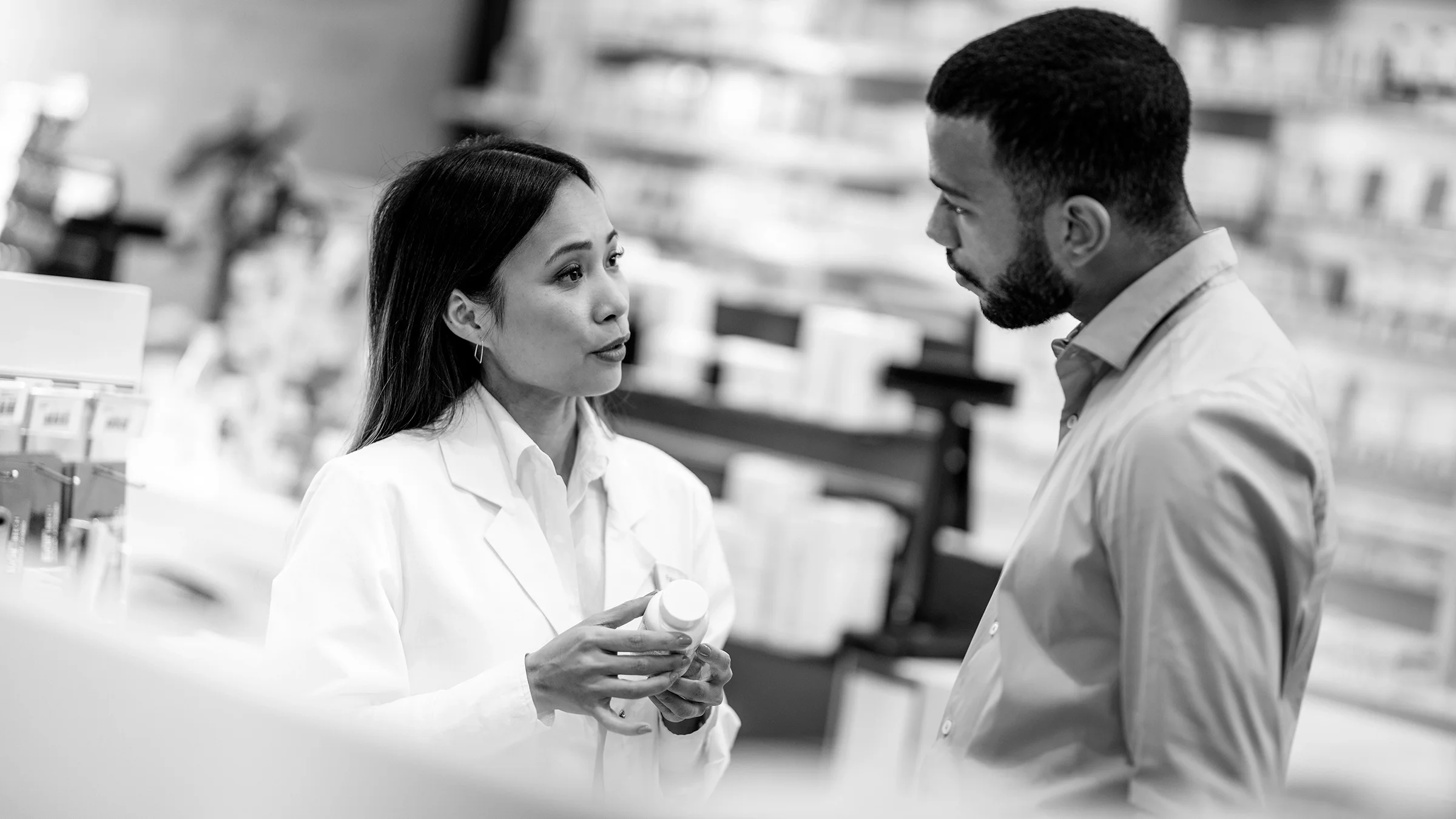 Black and white photo of a pharmacist helping a person in an aisle.