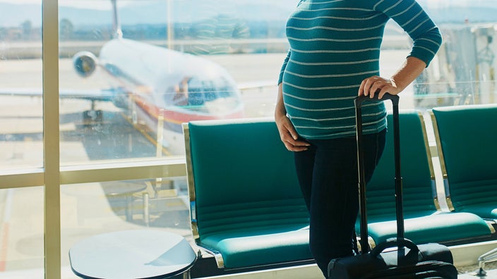 Pregnant woman at the airport with a rolling luggage.