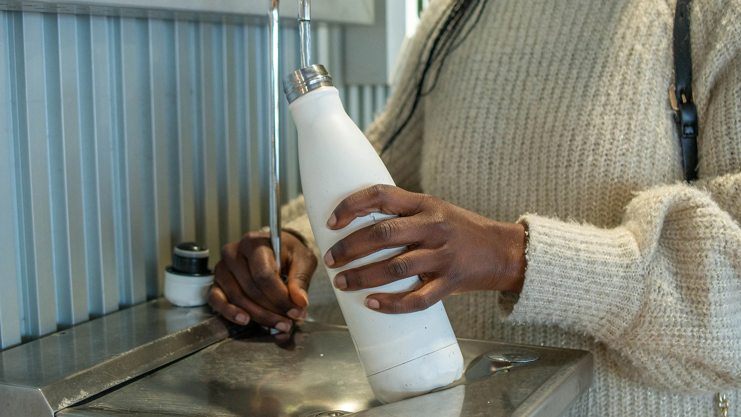 A woman refills a bottle at a water fountain.