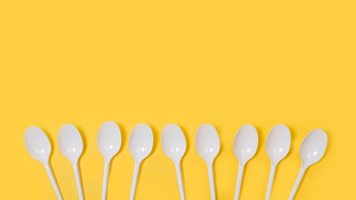 Nine plastic white spoons on a yellow background.