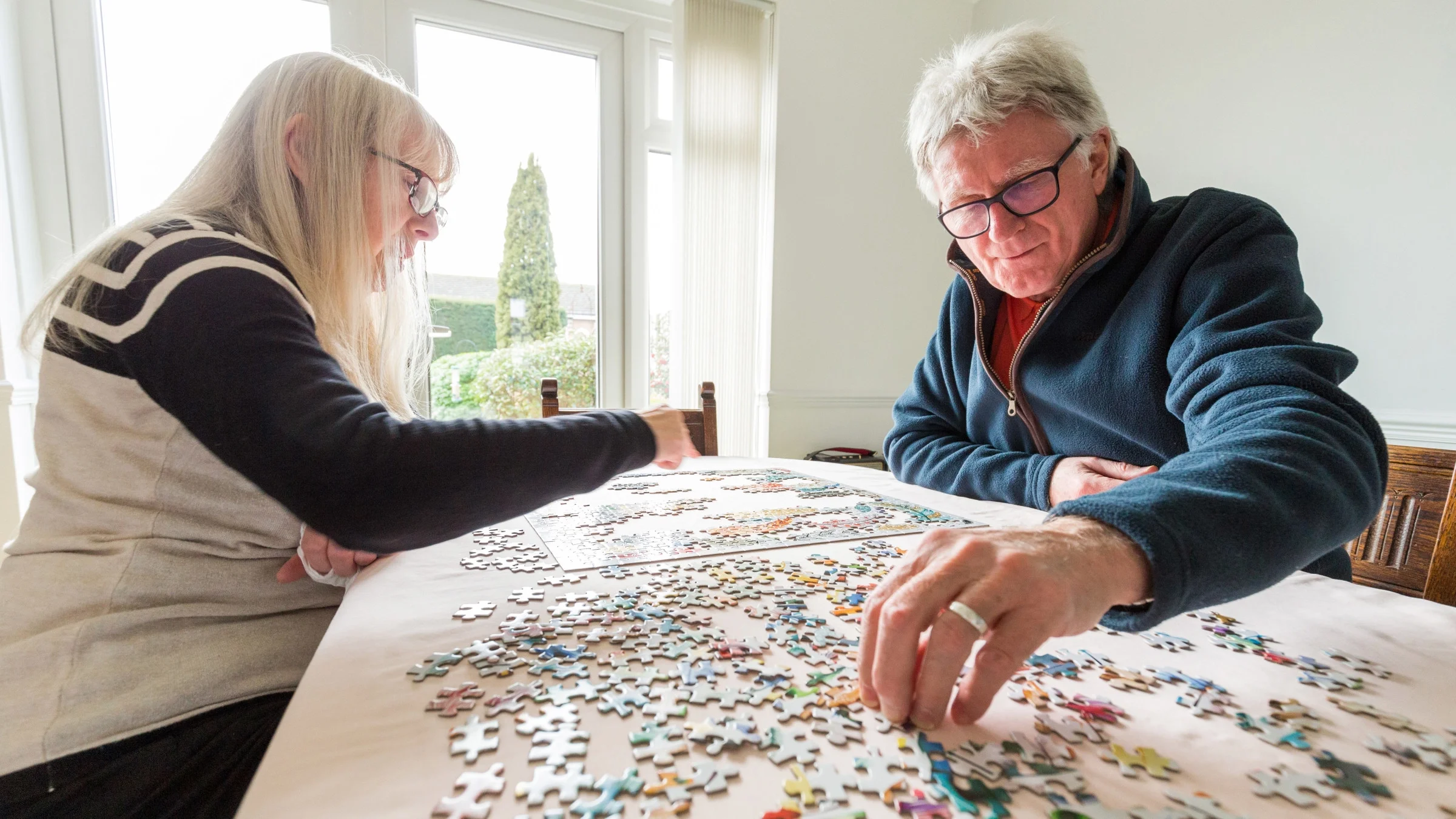 Retired couple with gray and white hair doing a puzzle together at home.