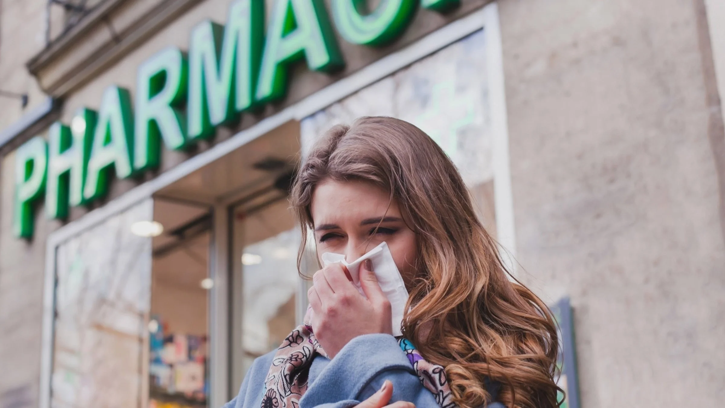 A person with allergies sneezing outside of a pharmacy.