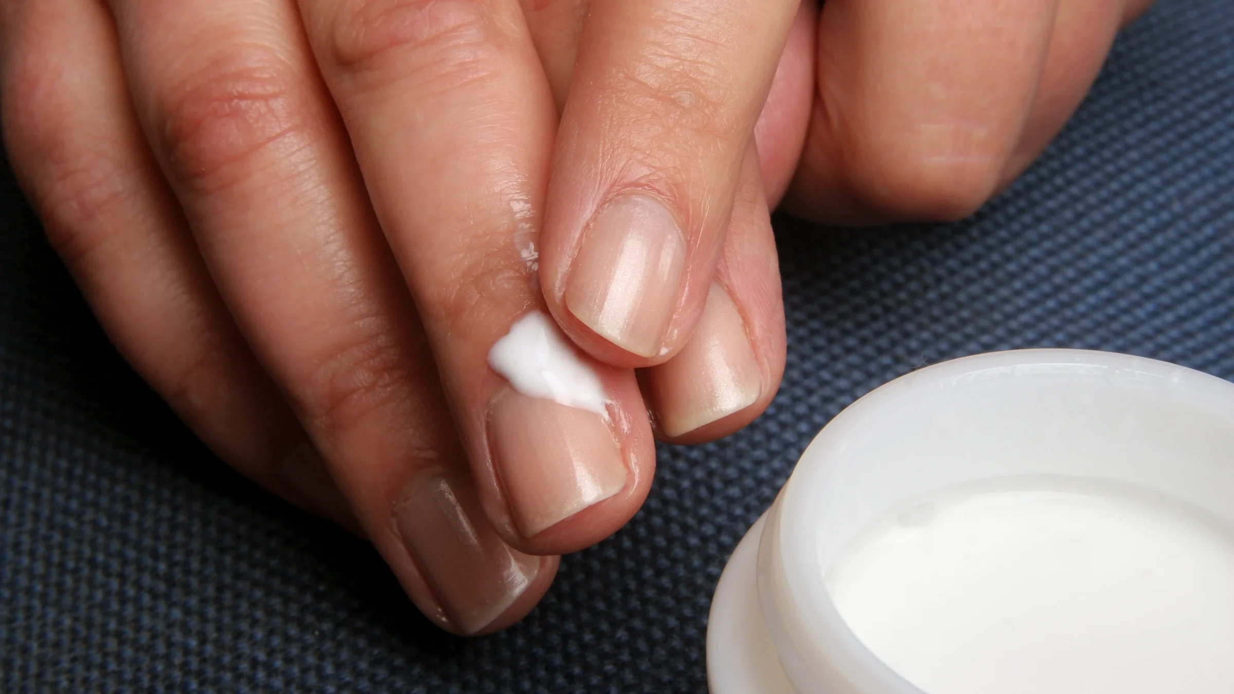 Close-up hands applying moisturizer to cuticles.