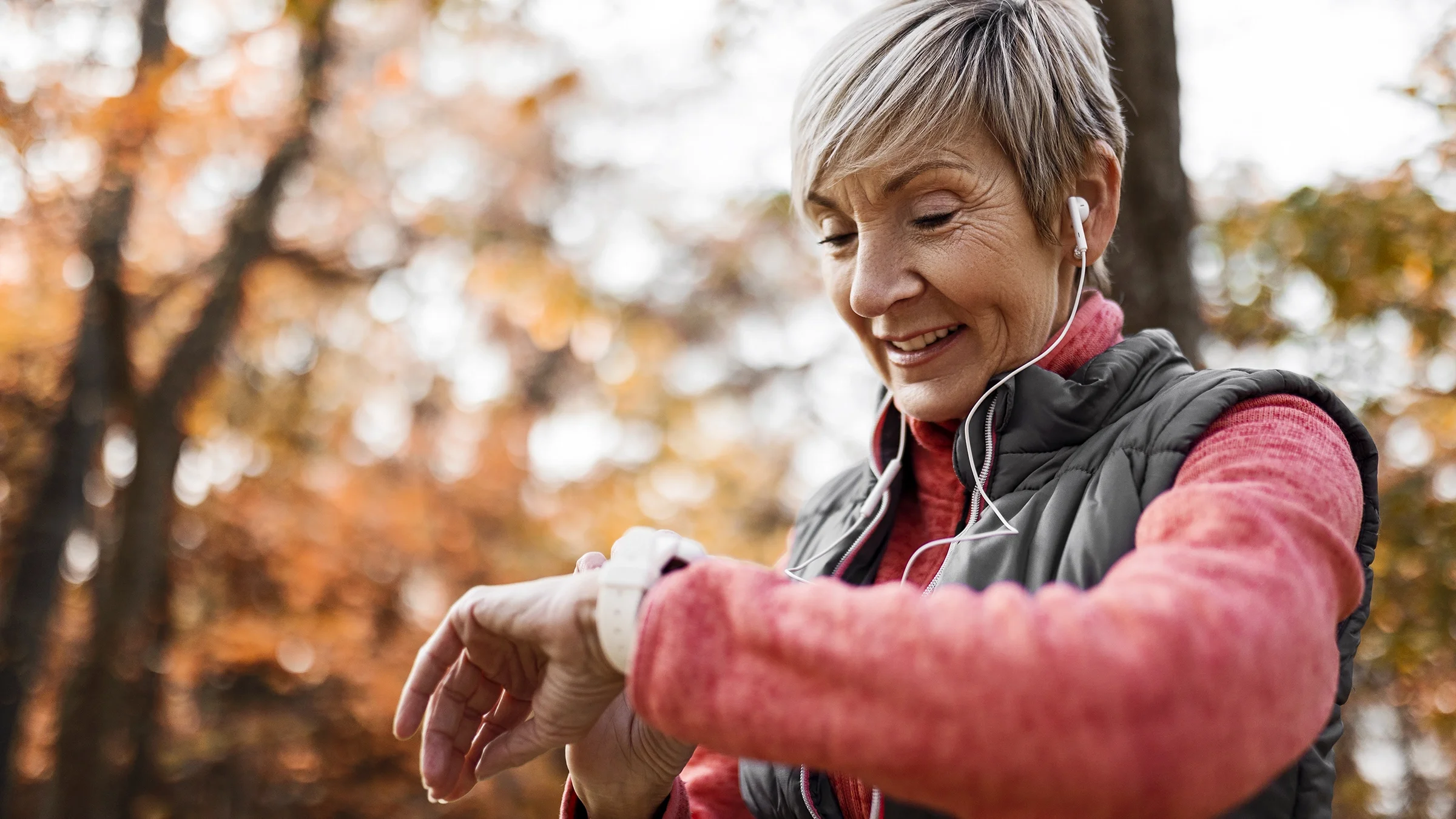 A senior woman looks at a smart watch while walking outdoors.