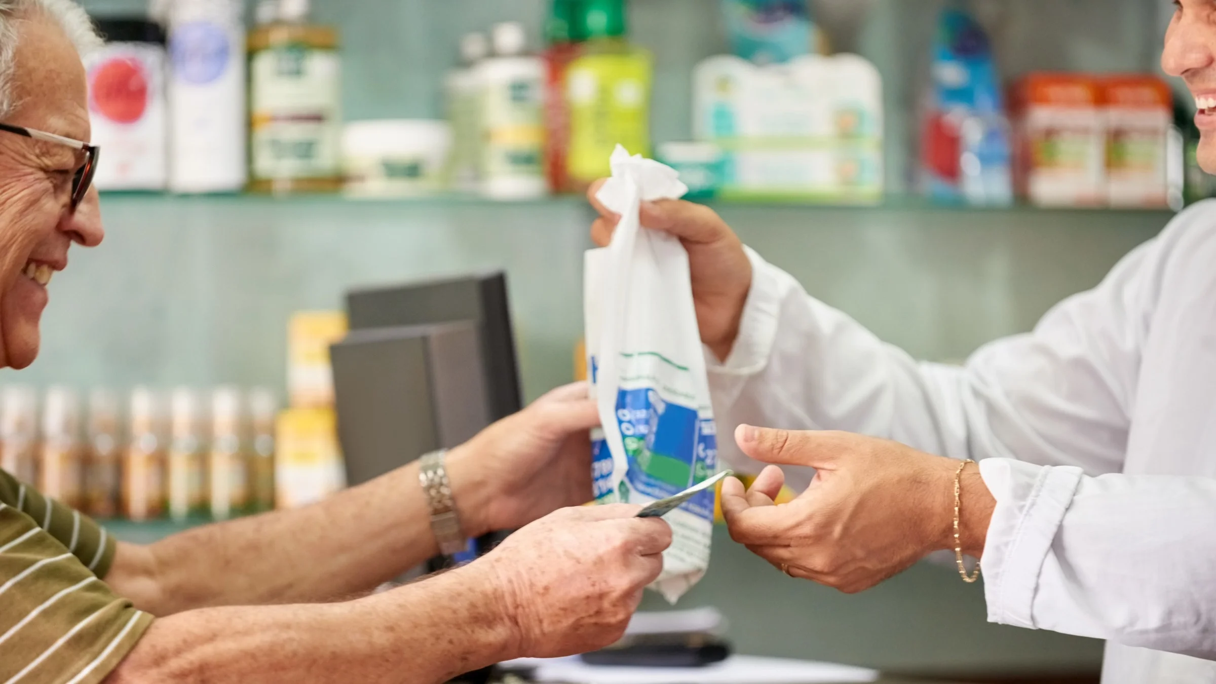 Elderly man smiling and paying cash for his prescriptions at the pharmacy counter.