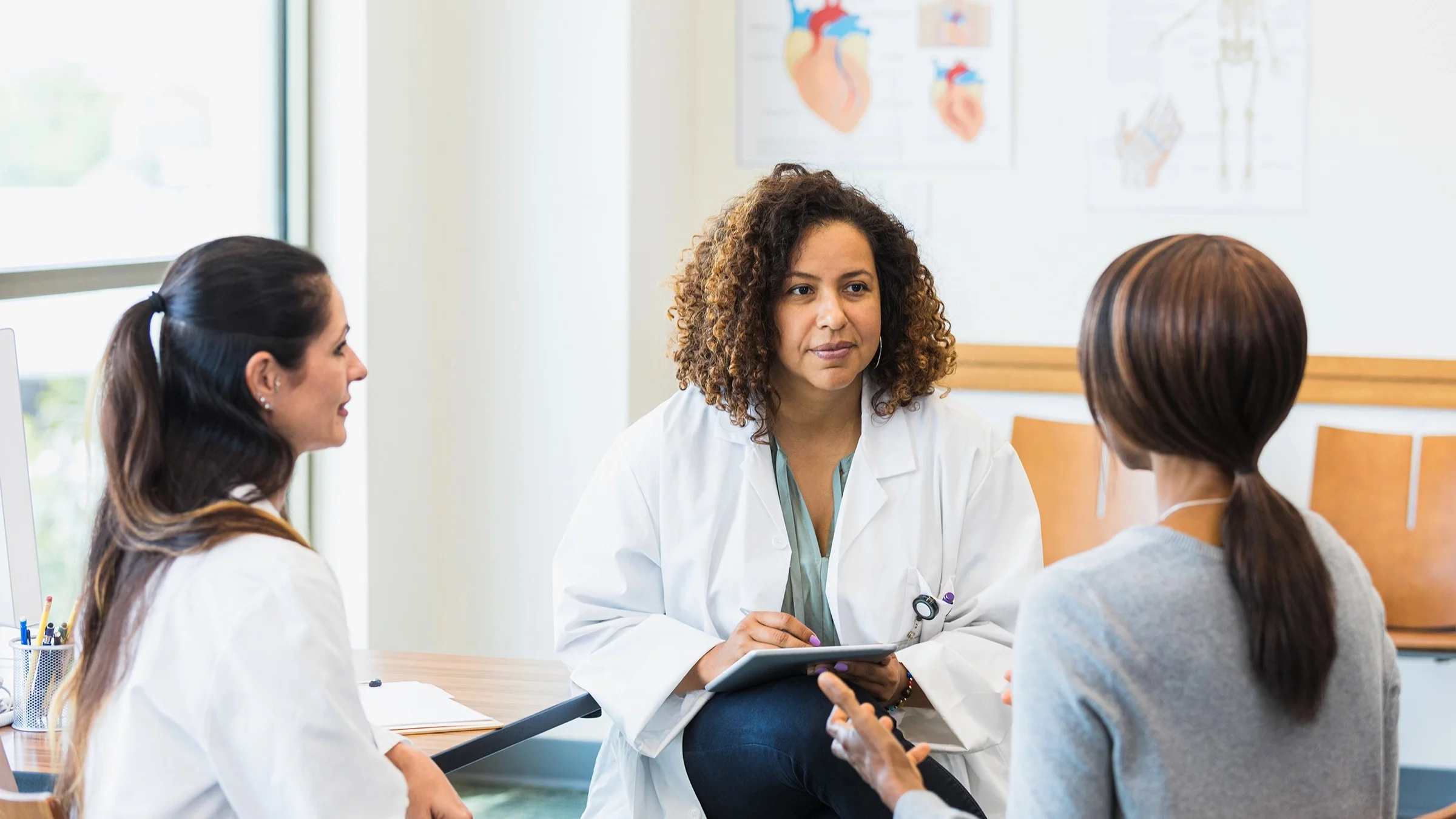 Female doctors listen to a female patient sitting down in their office.