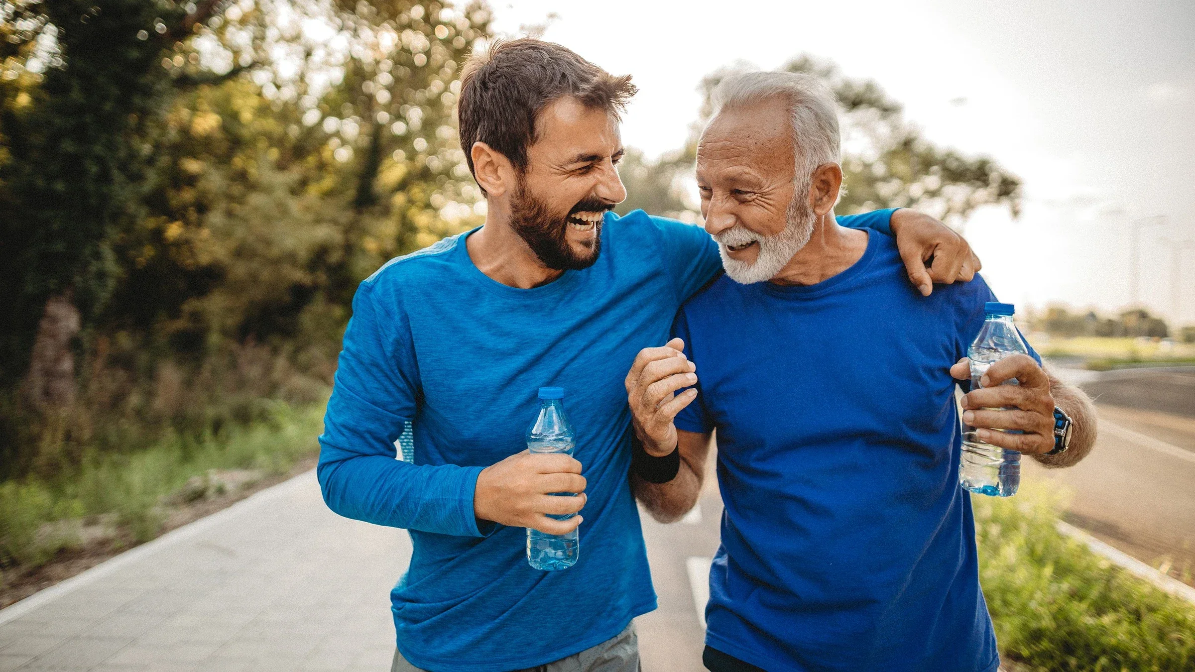 Father and son on a run together. They are both wearing bright-blue shirts and holding bottles of water. The father is older with gray hair and the son is middle-aged.
milan2099/E+ via Getty Images