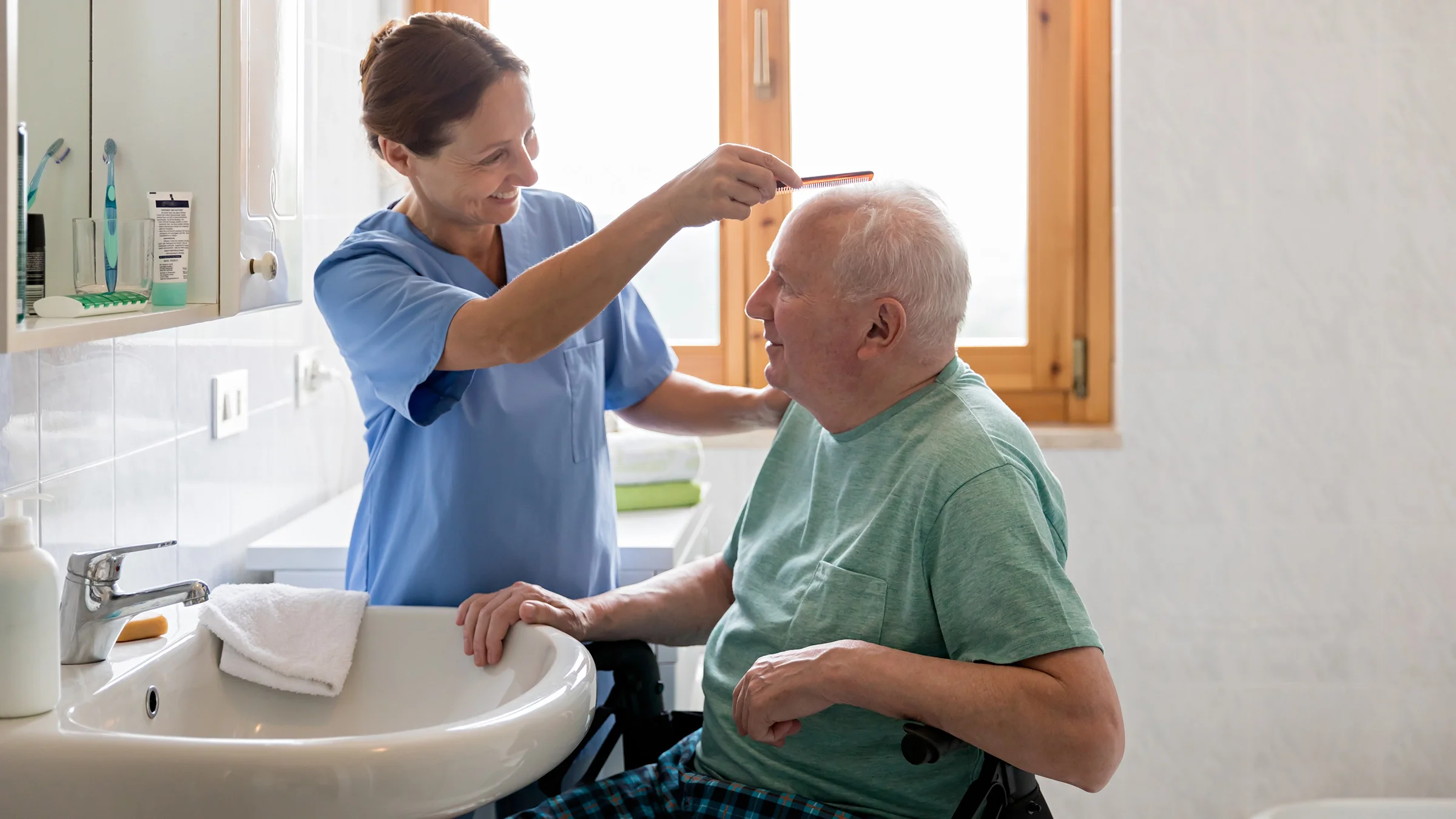 Nurse helping senior man get ready at home in the bathroom. Both are smiling.