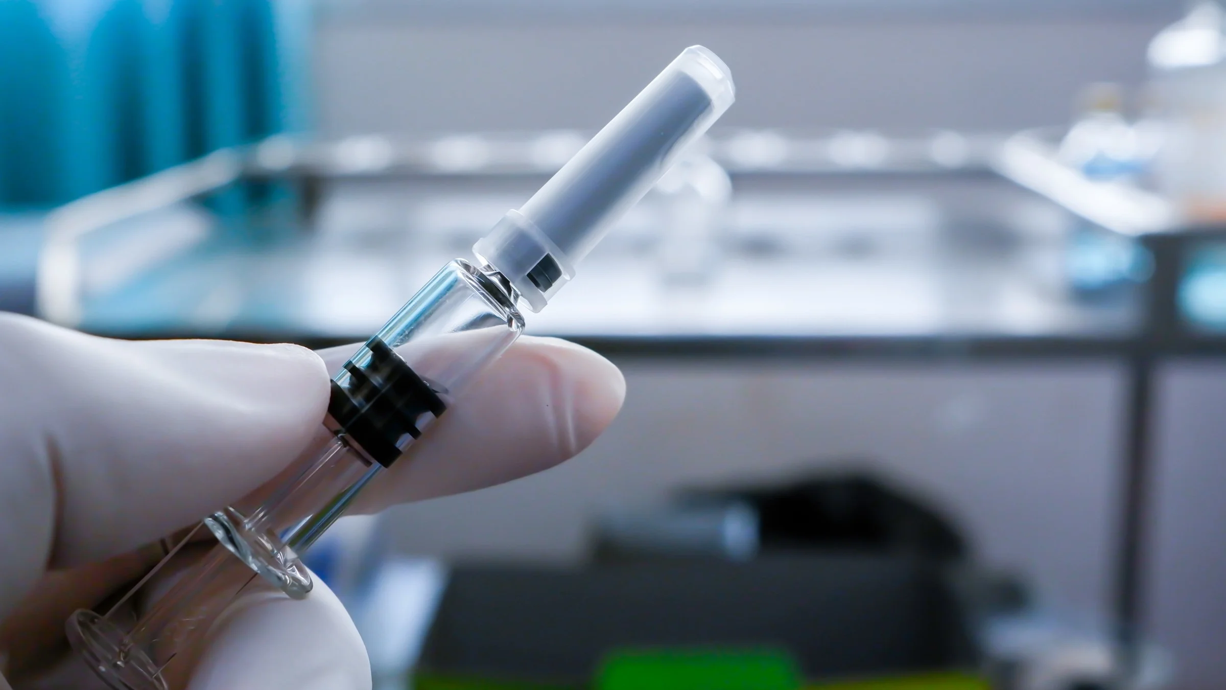 Medical syringe being held by a person in a white latex glove in a very clinical setting.