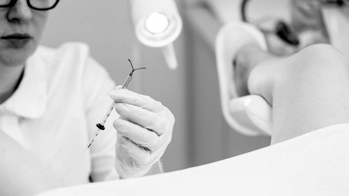 Gynecologist prepping an IUD for insertion into a patient. The patient is in the exam room with their legs in the stirrups.