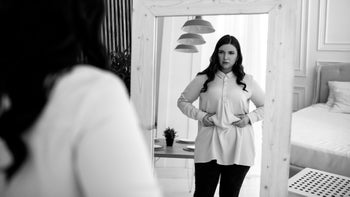 Health: Gut health: woman looking in full length mirror-1202795543