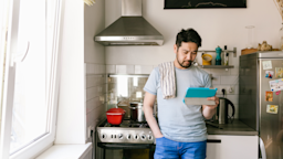 A man looks at a tablet while cooking. If you’re taking naproxen, there are certain foods you should avoid to prevent stomach irritation. 
visualspace/E+ via Getty Images